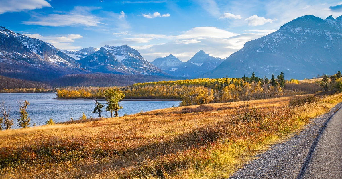 A roadside view of Glacier National Park in Montana with hills, a lake, and tall mountains in the background.