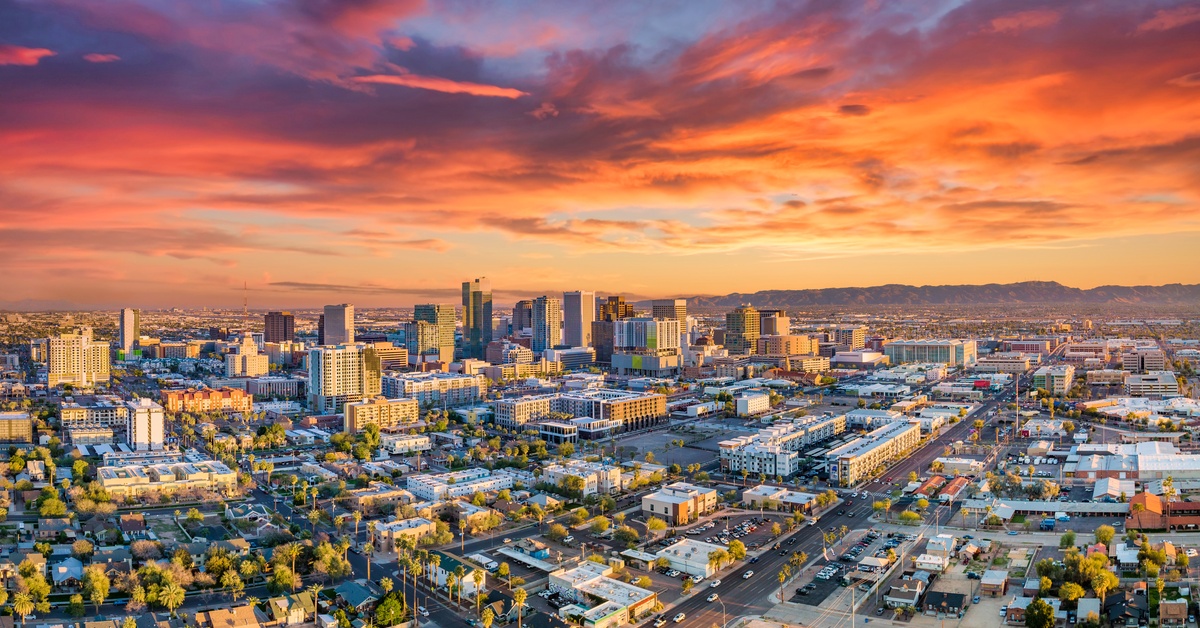 An aerial view of downtown Phoenix, Arizona at sunset. The city's skyline dominates the horizon line.
