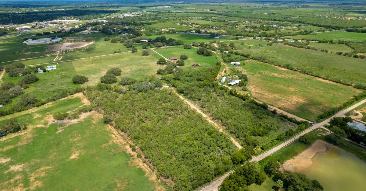 A view from above of some Texas farm land. There is a lone building surrounded by dense grassy areas.