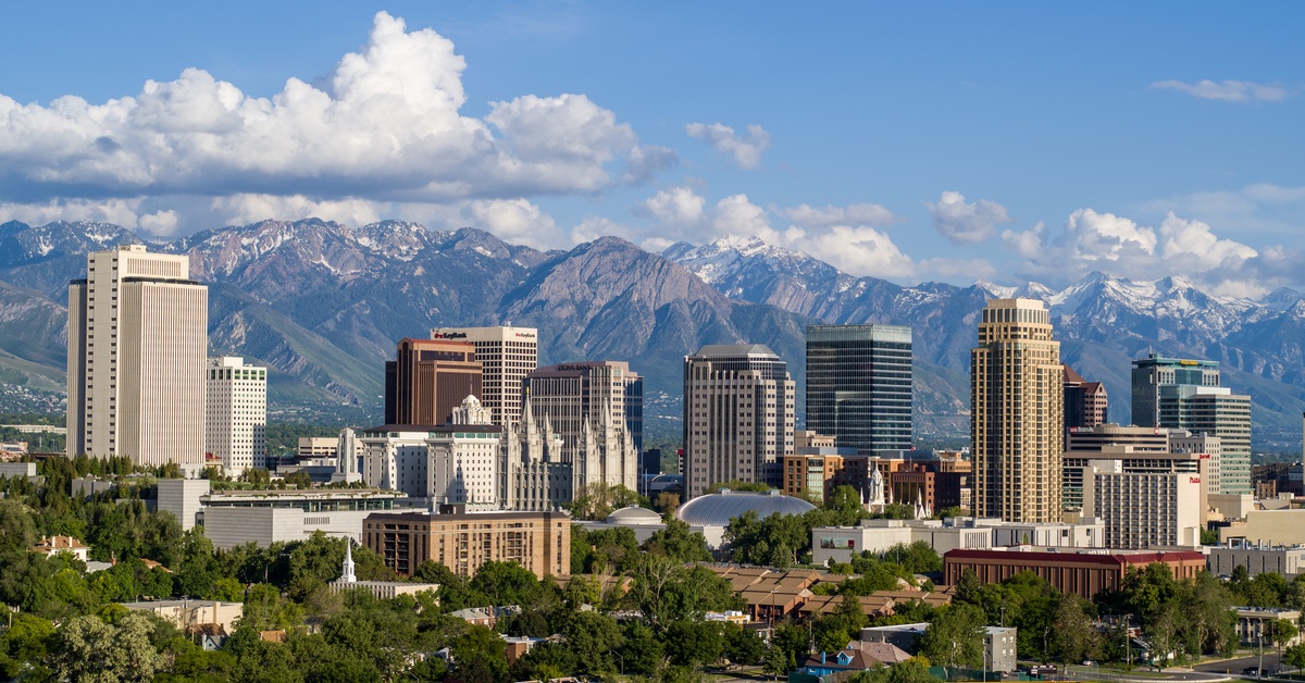 A distant view of the skyline of Salt Lake City, Utah. Behind the skyscrapers are large snow-capped mountains.