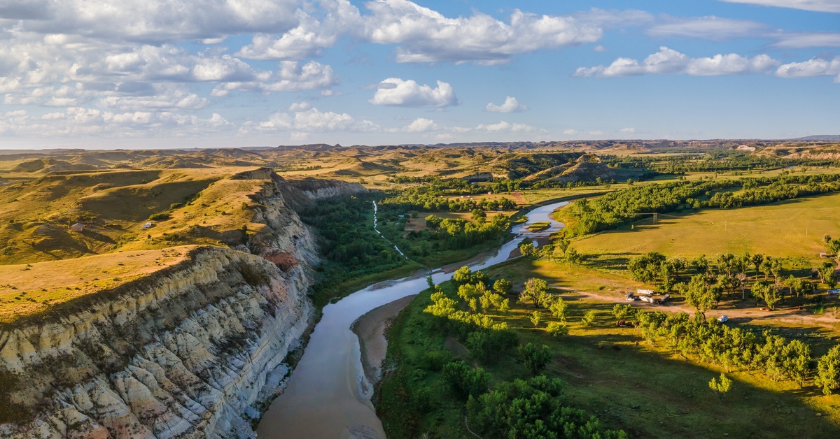 A view from the sky above a winding river in a canyon. Either side of the canyon are large open grasslands.