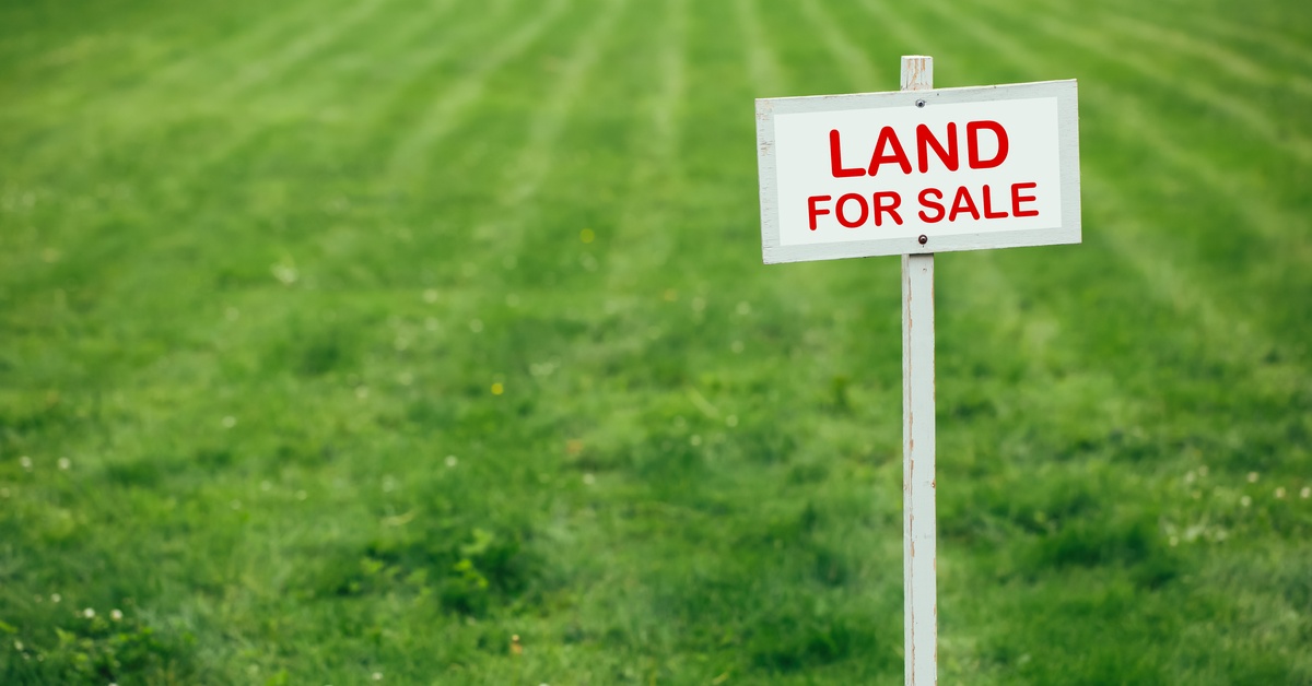 A small white sign with red lettering that says "land for sale." The sign is in front of a large grassy area.