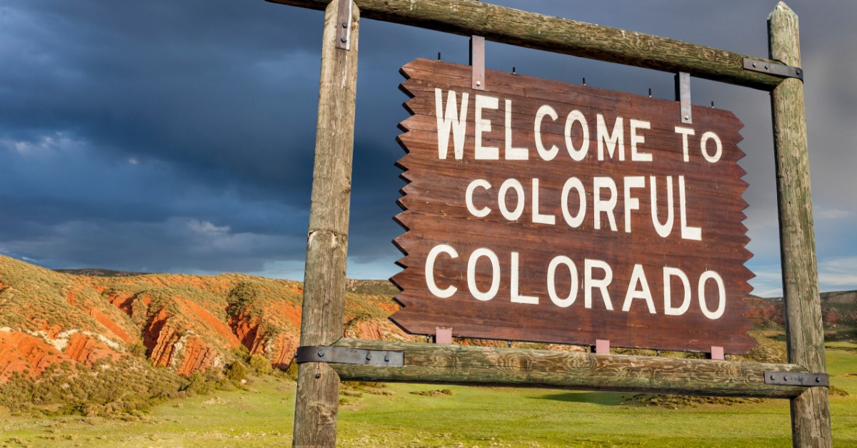 A closeup of a wooden sign that says, "Welcome to Colorful Colorado." The sky is cloudy behind the sign.