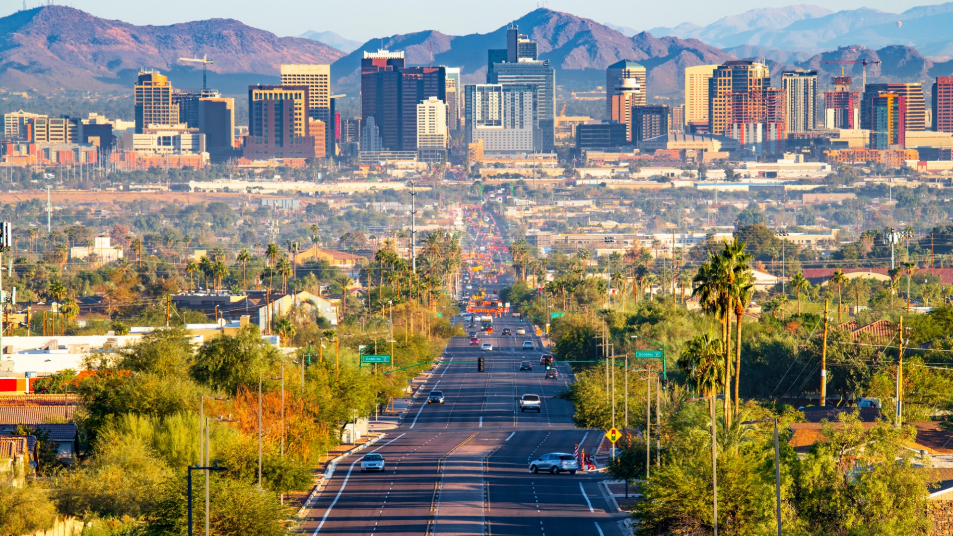The skyline of Phoenix, Arizona in the distance. There is a large, four lane highway heading straight towards the city.