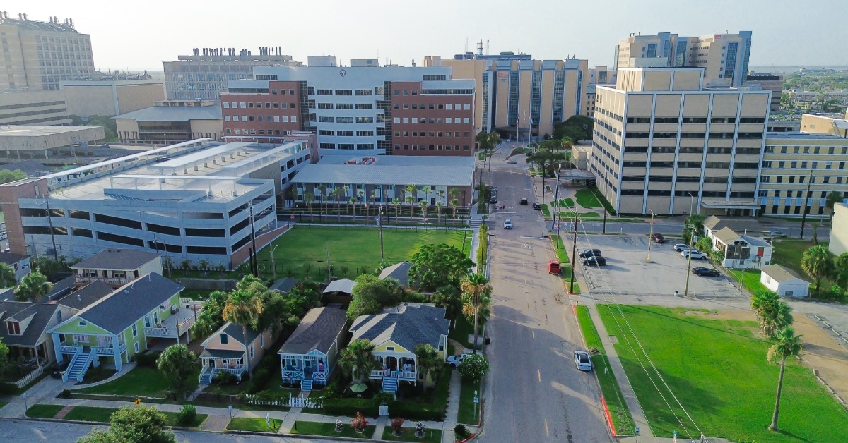 Several plots of open, grassy land positioned next to homes and buildings that are part of Galveston, Texas.