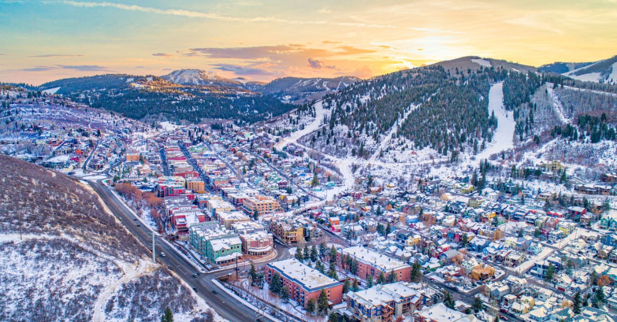 A drone view of Park City, Utah's downtown area. The buildings are stacked together in between two mountain ranges.