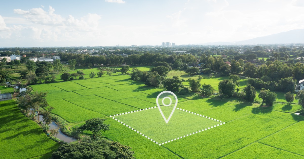 An aerial view of an open plot of land in the middle of a field. A white GPS marker and dotted line outline the plot.