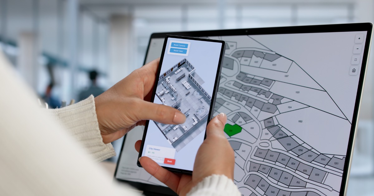A person holding a phone with a house blueprint in front of a screen depicting different zones for housing.