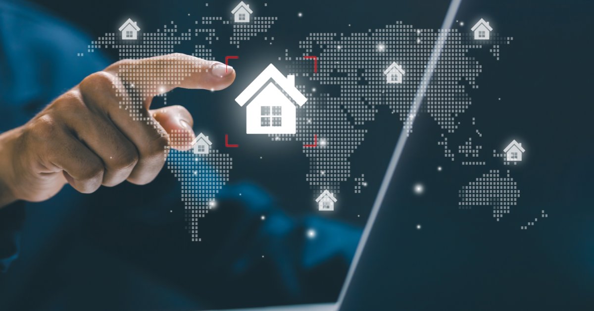 A person pointing at a laptop screen. A holographic picture of the world's continents and a house icon is above the screen.