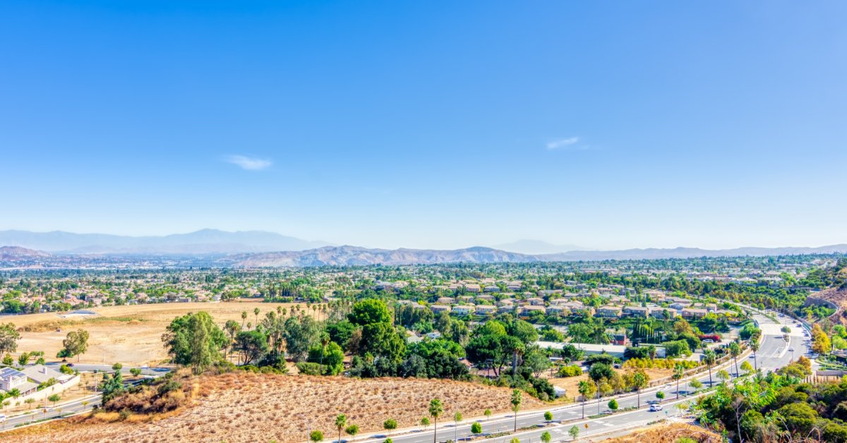 An aerial view of a highway in southern California. There are palm trees lining the street and in the neighborhoods.