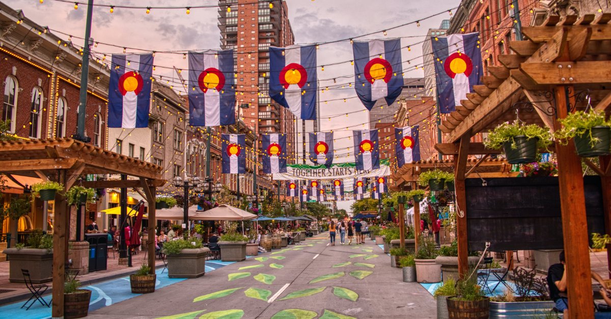 A city square with multiple pergolas on the street. Five Colorado flags are strung up on a line above the street.