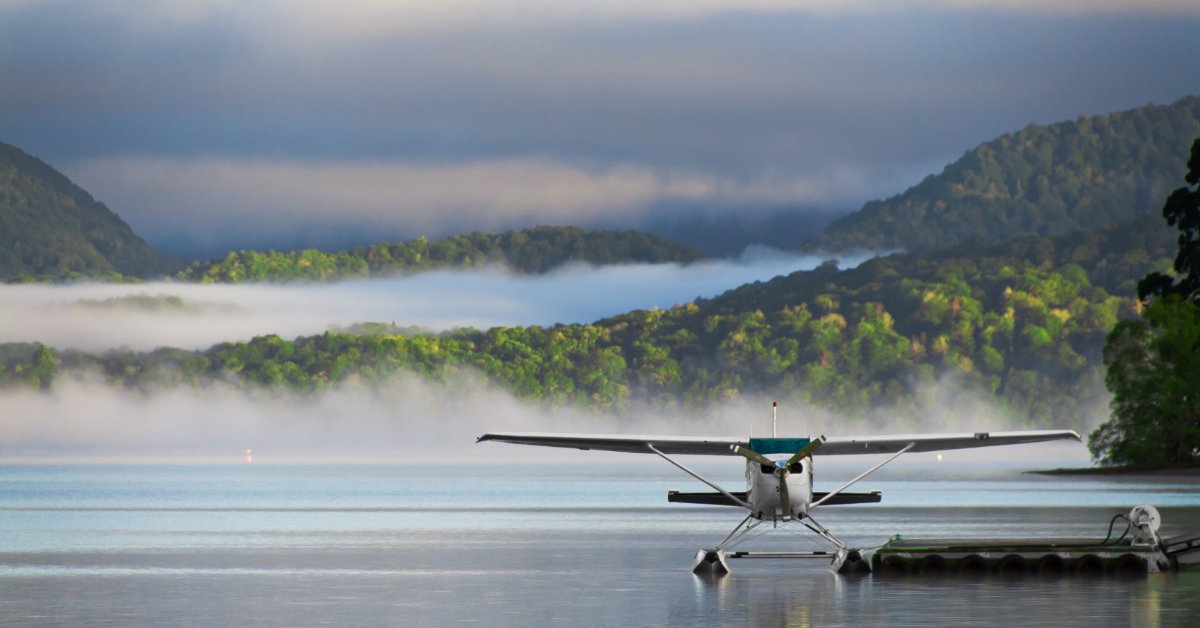 A waterplane parked at a small dock in the middle of a lake. There is a foggy forest in the distance beyond.