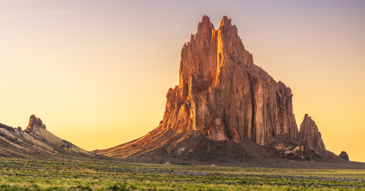 A wide open, arid field with small shrubs leading up to a large mountain in the distance in Shiprock, New Mexico.
