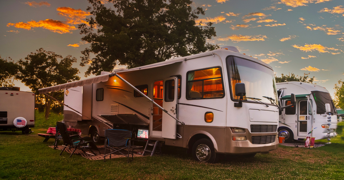 Large plot of land with multiple white RVs parked next to each other and some trees in the background during a sunset.