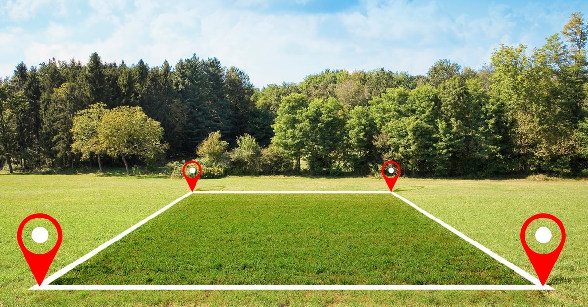 A white square with red location arrows in each corner overlays a plot of land covered in green grass.