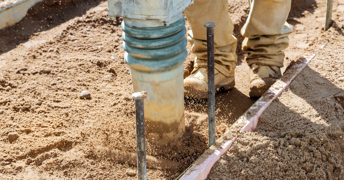 Close-up of the feet of a construction worker using a large rammer to compact the soil around a construction area.