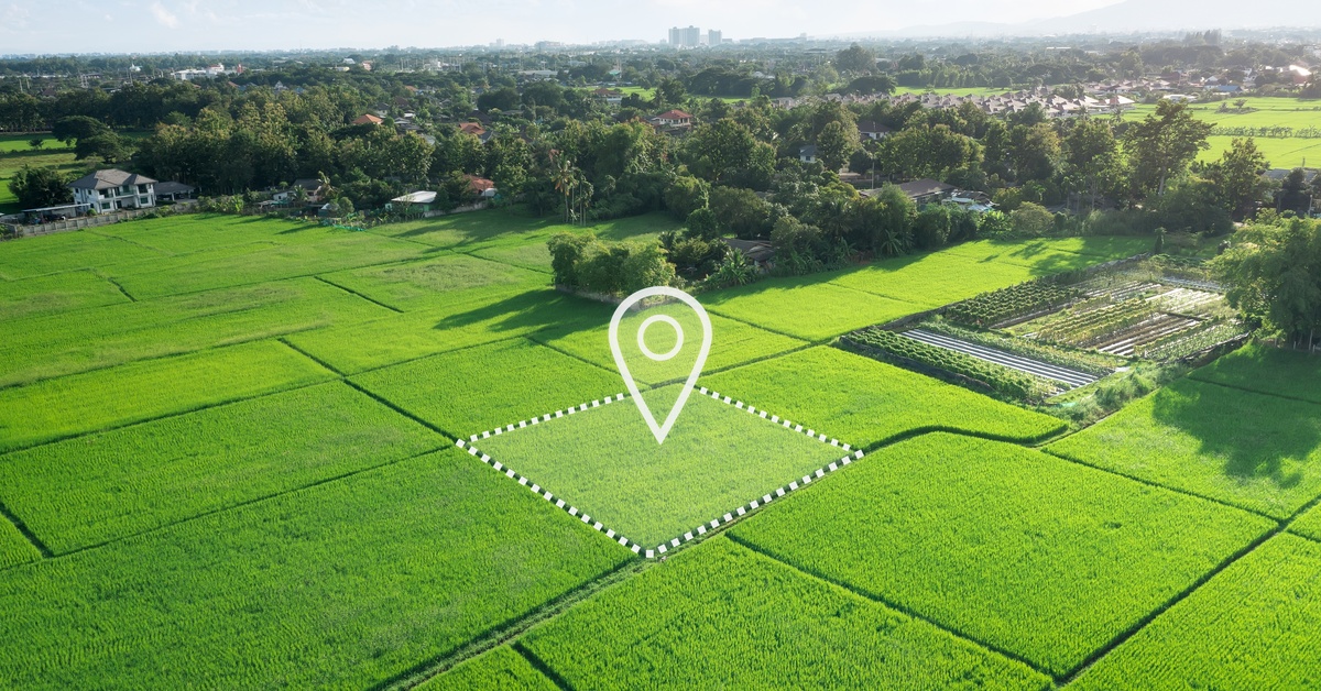 An aerial view of a large plot of farmland divided into smaller lots, with one showing a digital pin in the middle.