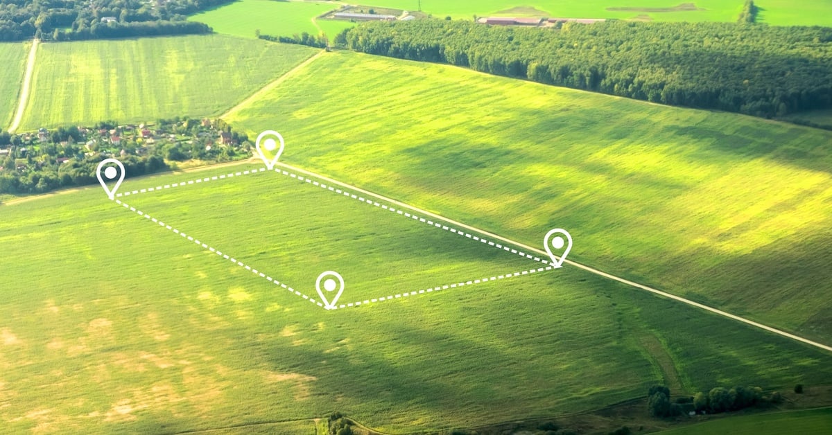 A large plot of land covered in lush grass, showcasing a potential property via digital dotted white lines and four pins.