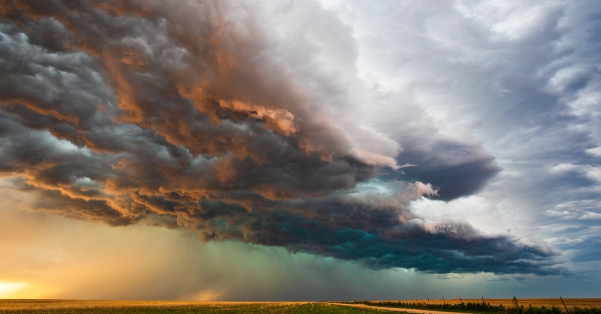Plot of land with a dirt road on the right side under a large black stormy cloud with rays of light breaking through.